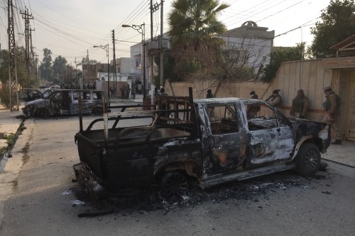 Soldiers line a street filled with burnt-out vehicles.