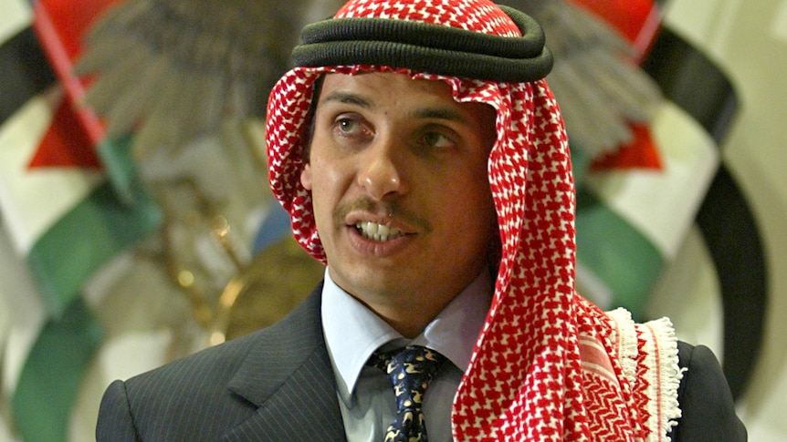 A man in a suit wearing a keffiyeh in front or a Jordanian emblem.