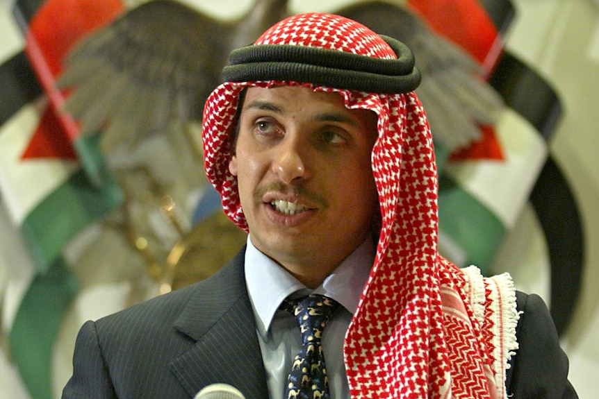 A man in a suit wearing a keffiyeh in front or a Jordanian emblem.