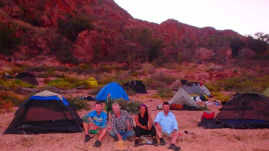 Four participants of a leadership course sit beside their tents in a remote campground