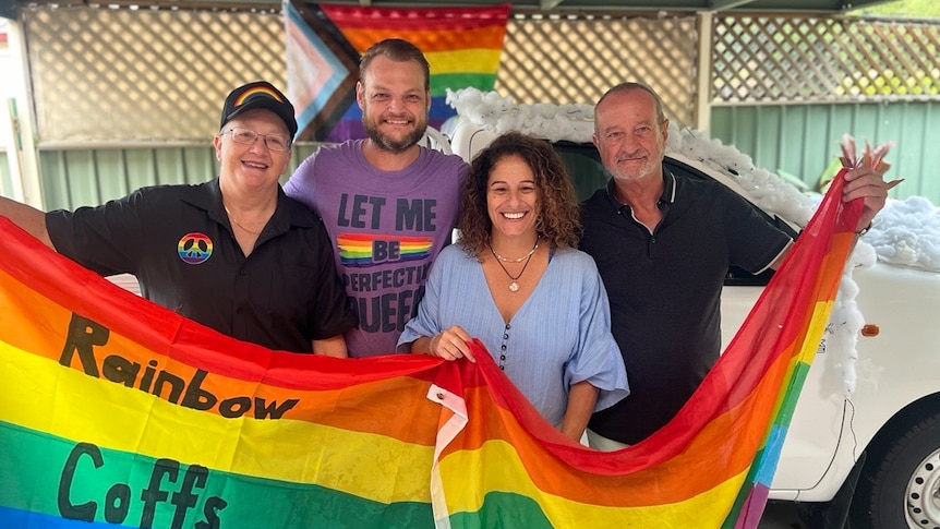 four people from LGBTQI+ group rainbow coffs harbour smiling with rainbow flags