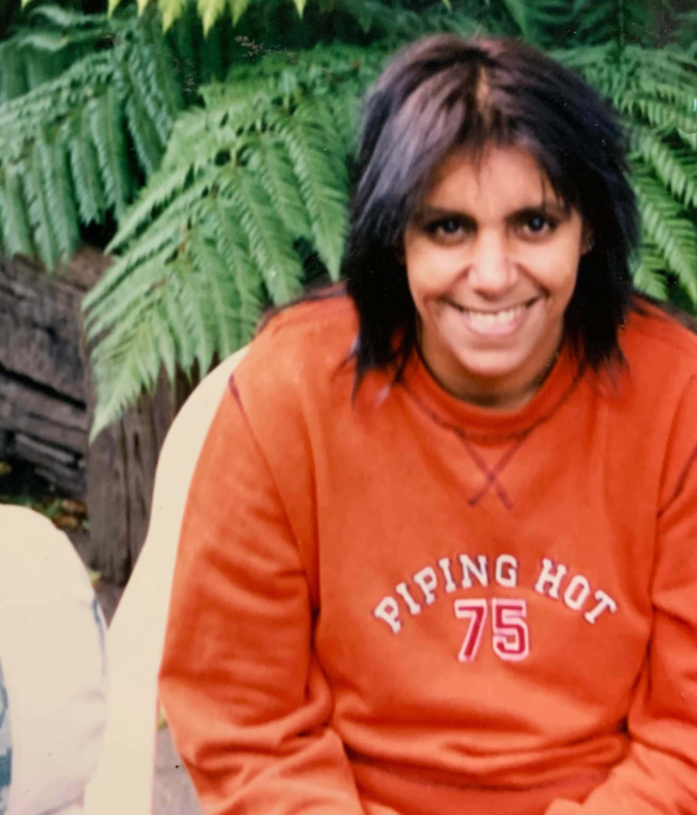 A smiling woman sitting outside wearing a bright orange sweat shirt.