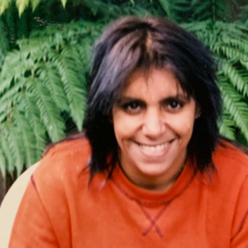 A smiling woman sitting outside wearing a bright orange sweat shirt.