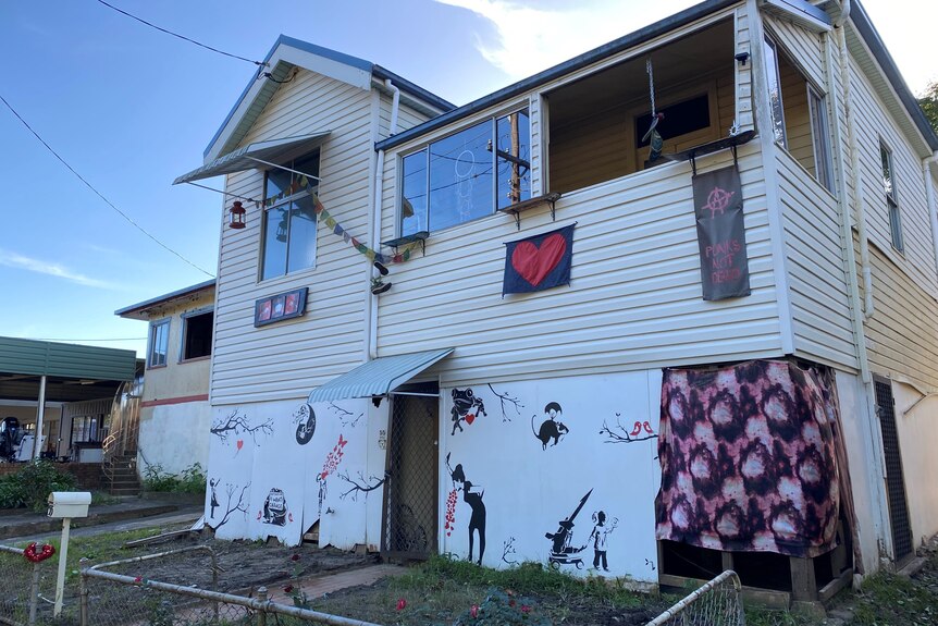 A house decorated with black and red artwork and coloured flags. A window and some sections of drywall are missing.