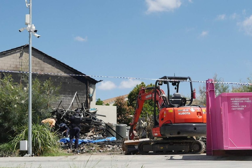 A bulldozer in front of rubble where police officers look through.