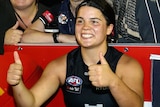 Madison Prespakis smiles and gives a double thumbs up while standing near a crowd of happy Carlton fans.