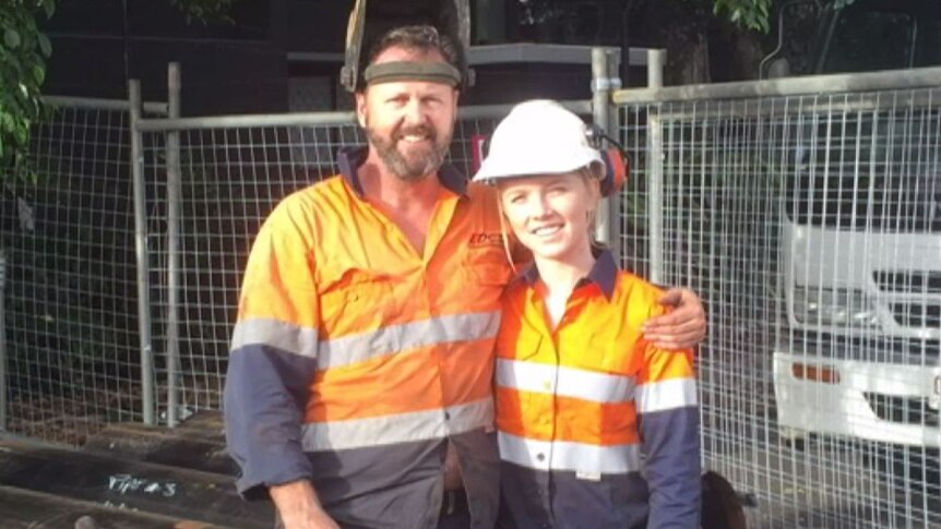 A young woman and her father pose for a photo wearing high-vis orange workwear