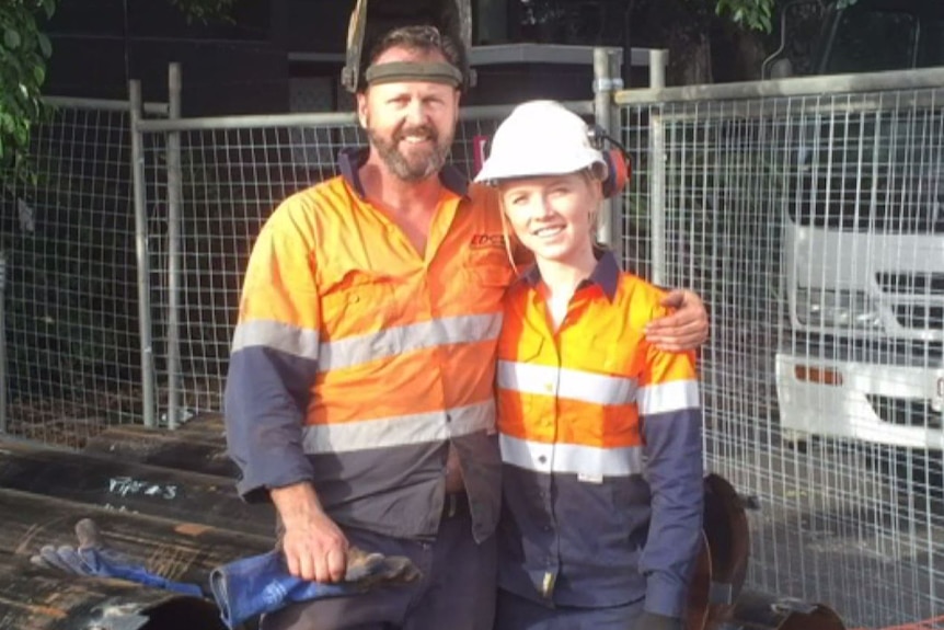 A young woman and her father pose for a photo wearing high-vis orange workwear