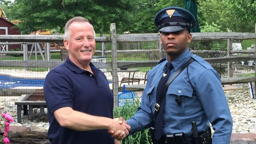 Trooper Michael Patterson in uniform shakes the hand of an older white male in plain clothes