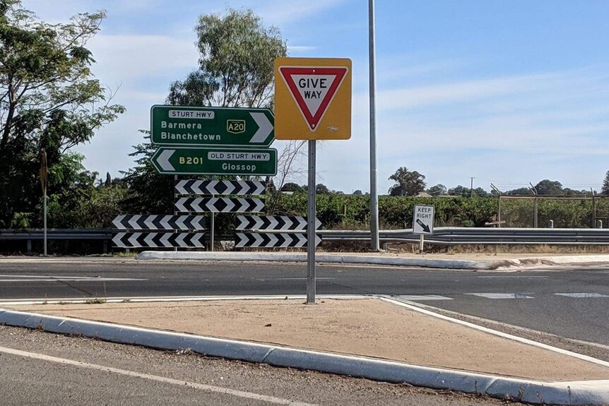 Una señal de carretera de direcciones junto a la carretera, detrás de una señal de ceder el paso