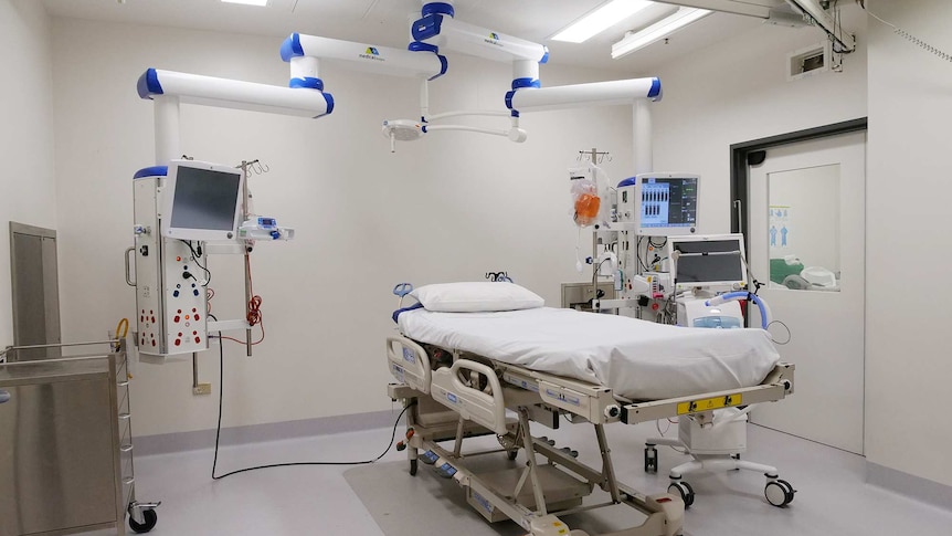 A white room filled with an ICU bed, several monitors and other medical equipment