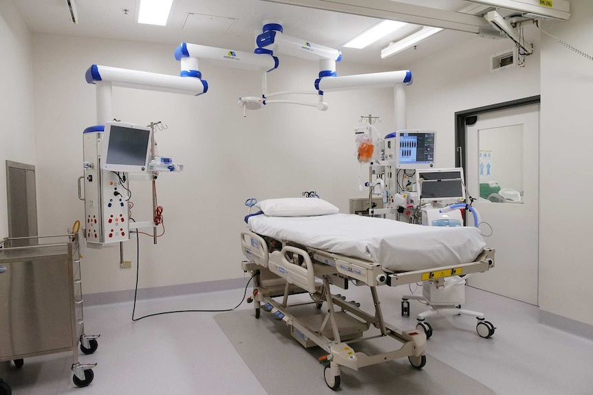 A white room filled with an ICU bed, several monitors and other medical equipment