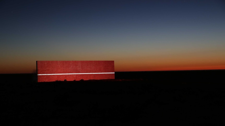 An image of a red brick wall projected on to another wall in the middle of the desert at sunrise.