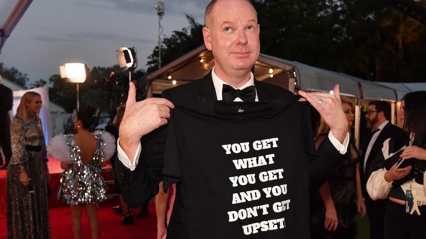 Tom Gleeson on the red carpet wearing a shirt that says "you get with you get and you don't get upset".