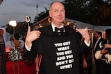 Tom Gleeson on the red carpet wearing a shirt that says "you get with you get and you don't get upset".