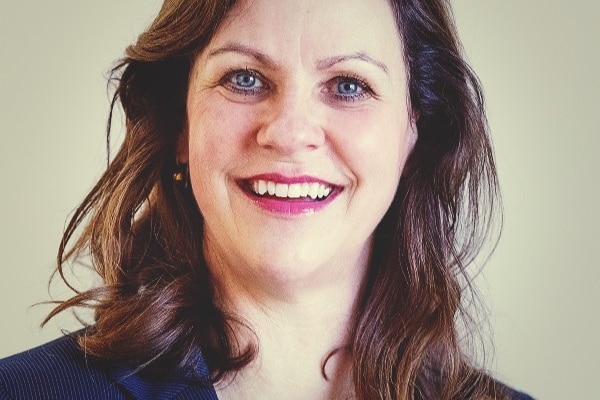 A smiling woman with shoulder-length brown hair wearing a black blazer.