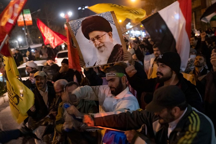 Protesters in Tehran tear an Israeli flag up.