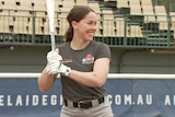 A woman smiling holding a baseball bat. 