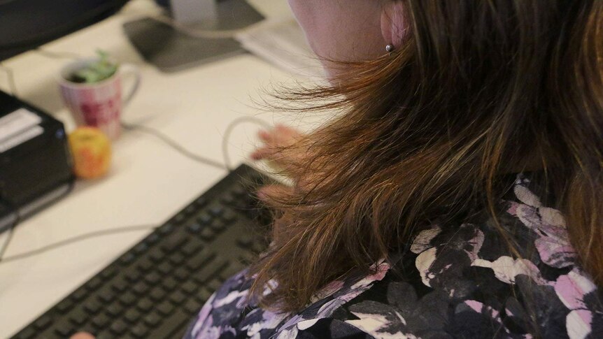 A woman, face unseen typing on a computer keyboard at a desk