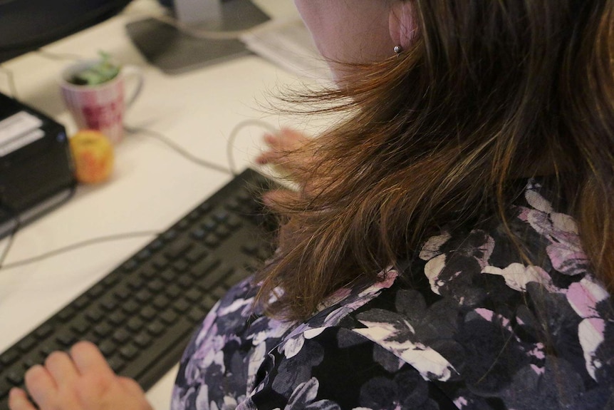 A woman, face unseen typing on a computer keyboard at a desk