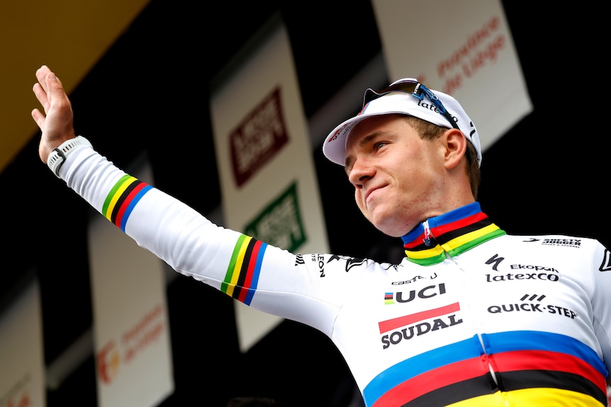 Remco Evenepoel waves while wearing a long-sleeved rainbow jersey
