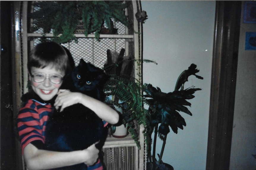 A young boy in glasses holding a black cat.