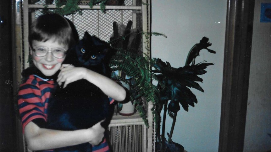 A young boy in glasses holding a black cat.