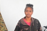 An Aboriginal woman stands outside a tent. She has a serious expression on her face.