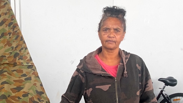 An Aboriginal woman stands outside a tent. She has a serious expression on her face.