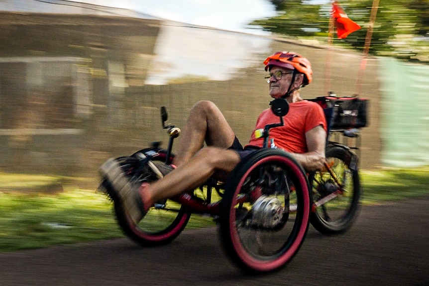 Blurred image of man in lane way at speed on recumbent tricycle.