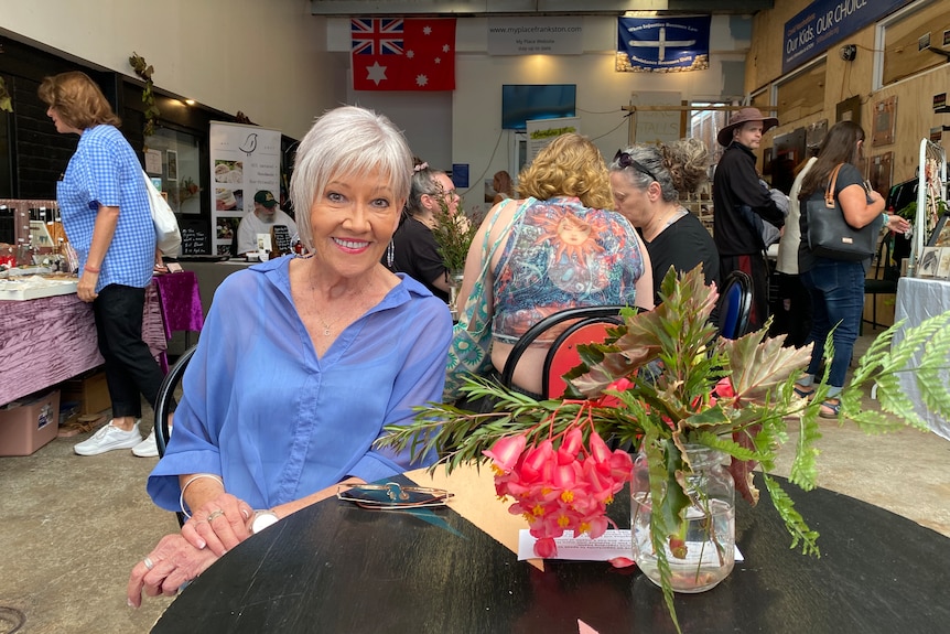 A woman sits at a table with a vase of flowers on it.