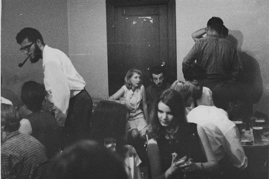 Black and white photo of people sitting around chatting in a pub