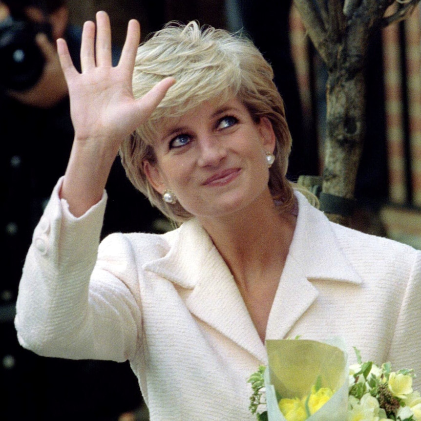 Princess Diana in a cream suit and pearl earrings smiles as she waves and glances up. She clutches bouquets of flowers