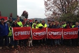 Workers are standing outside the locked-down ply  mill with banners in protest
