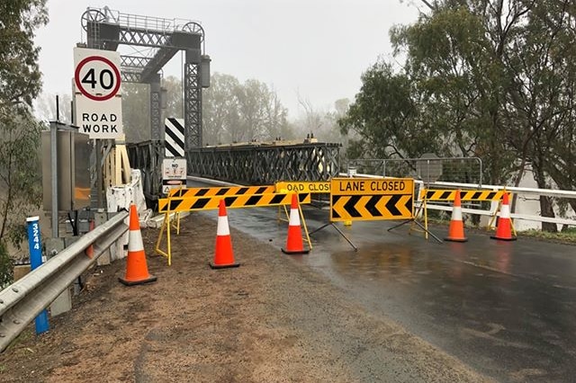 "Road closed" signage blocking the entrance to an old steel bridge.