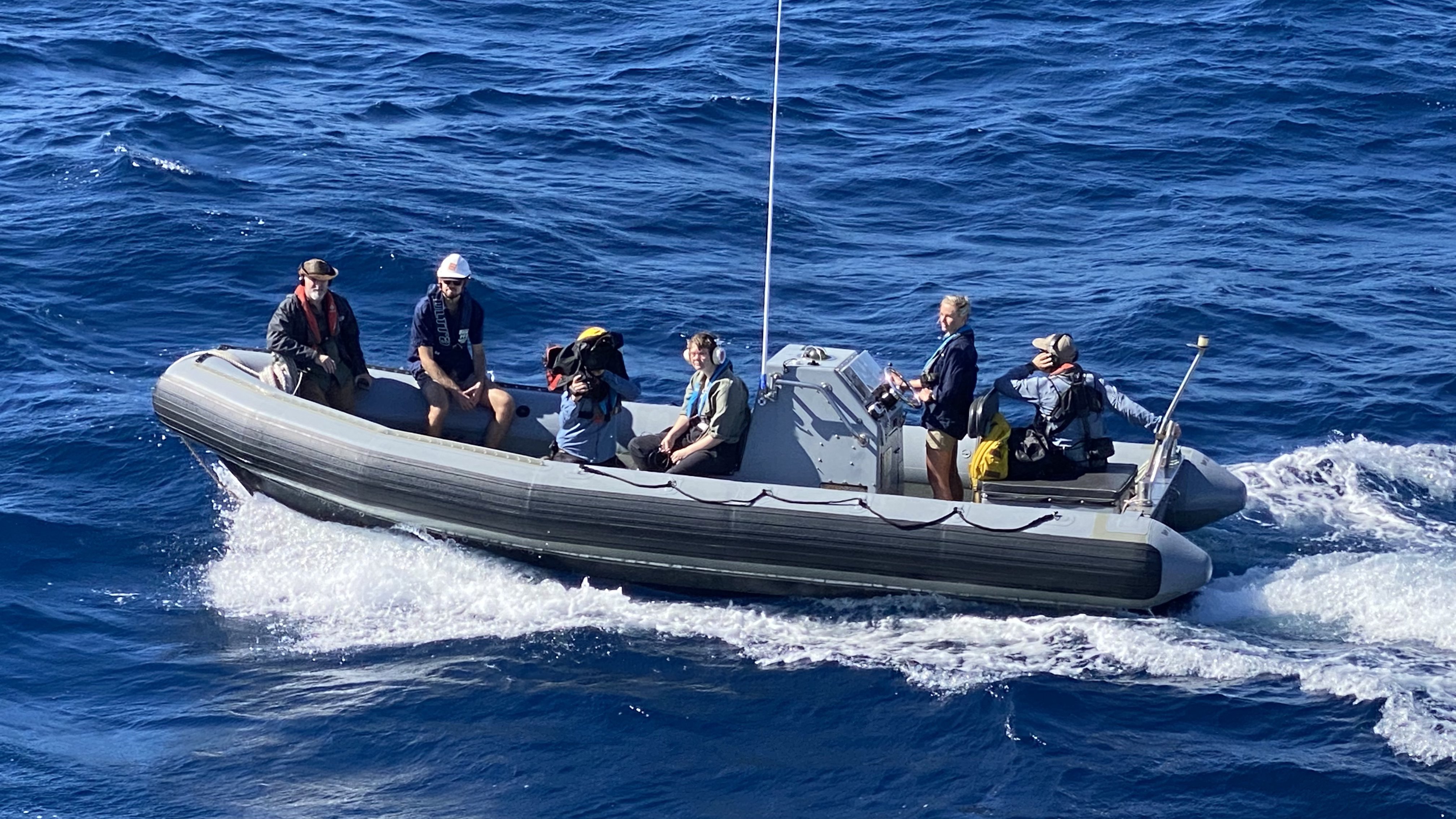Aerial shot of camera crew and other people in a dinghy on water.