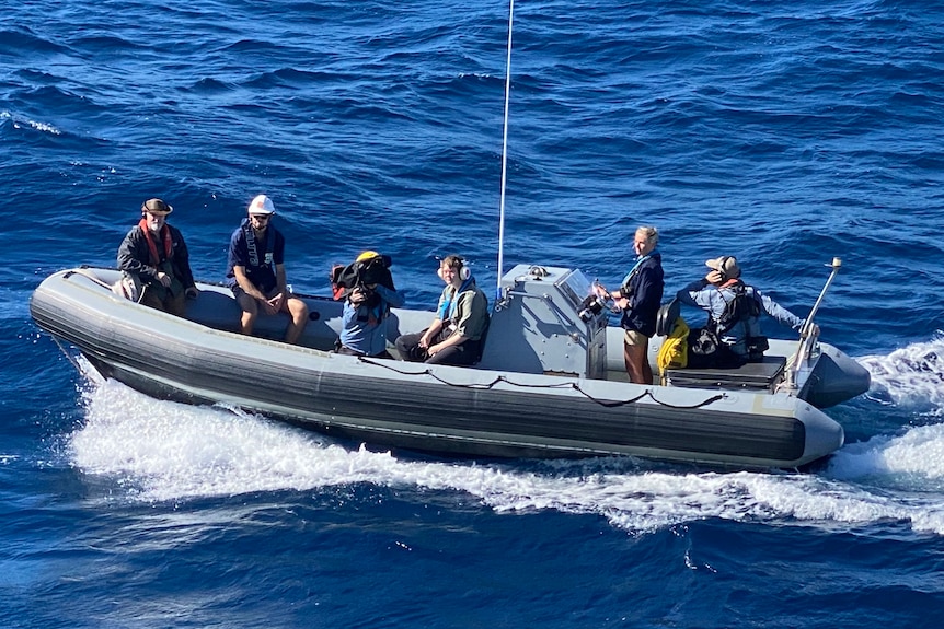 Aerial shot of camera crew and other people in a dinghy on water.