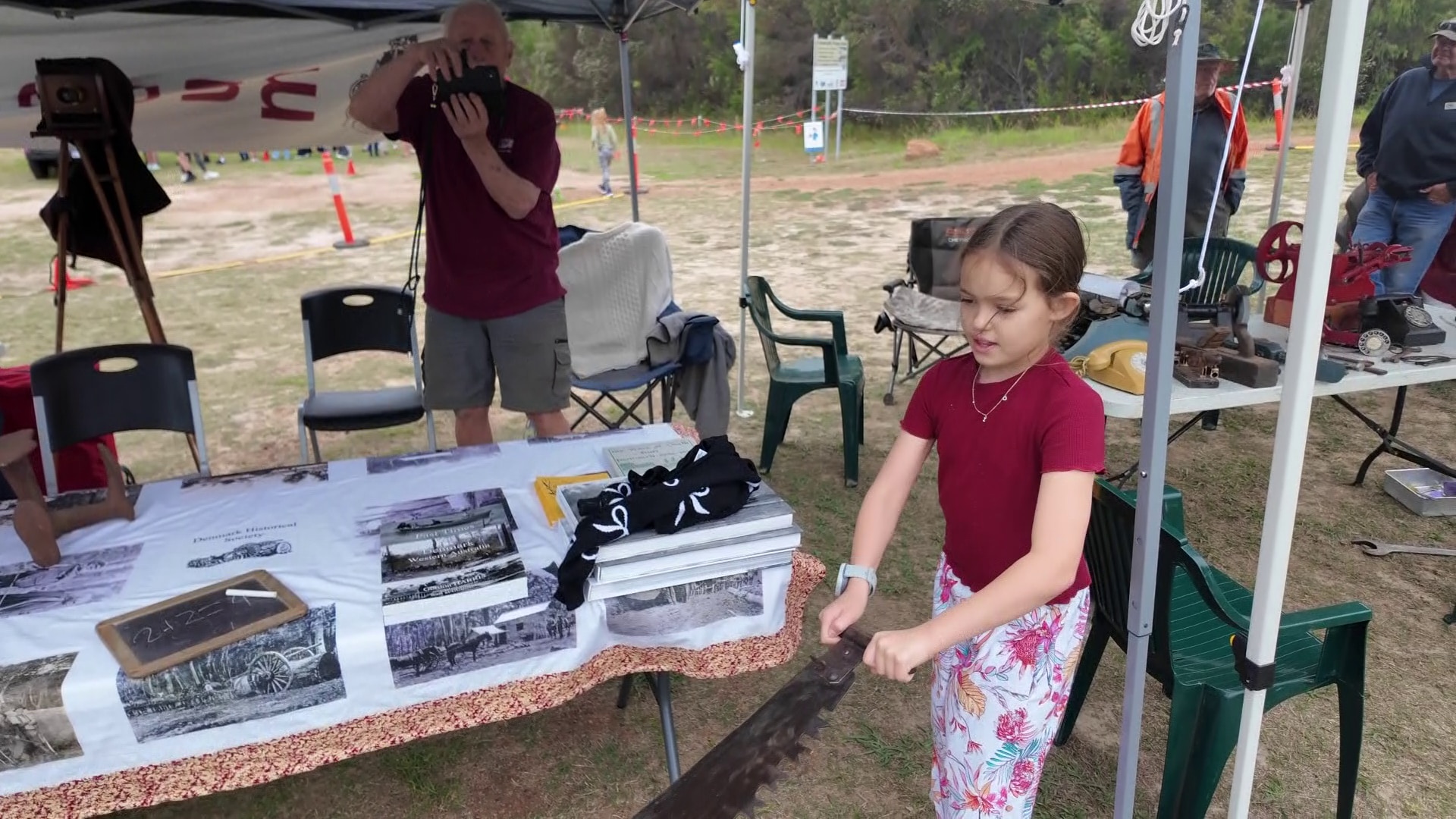 Una joven sostiene el extremo de una sierra para dos hombres.