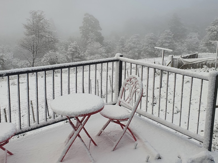 Snow covers a timber deck and outdoor table and chair