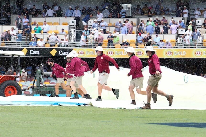 six men pulling a tarp over a cricket pitch