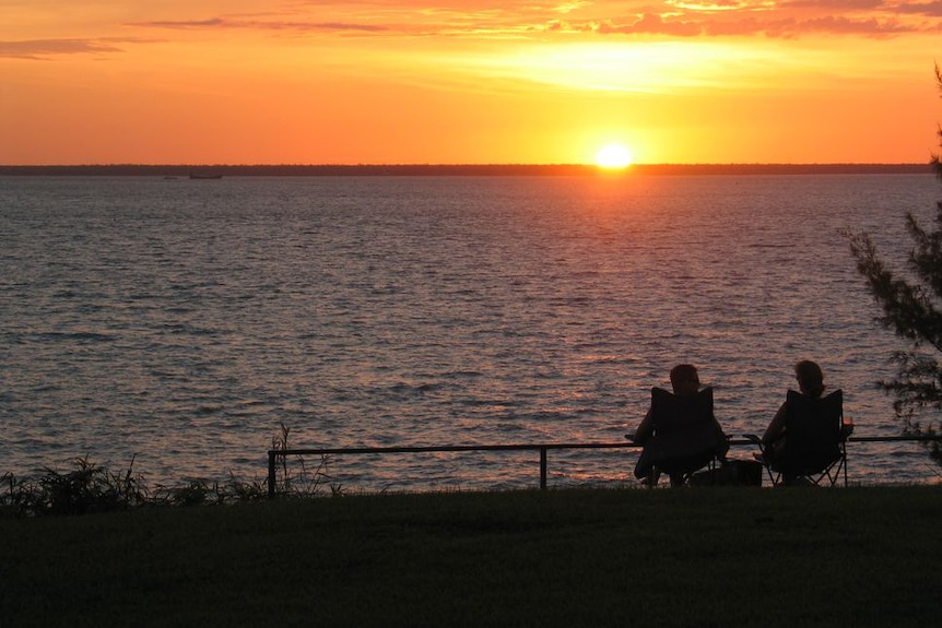 The silhouette of two people in camp chairs as they watch the sunset from the coastal Darwin suburb of Fannie Bay.