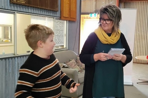 A boy gestures as he speaks to a middle-aged, bespectacled woman.