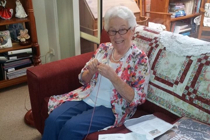 An elderly woman sitting on a couch knitting