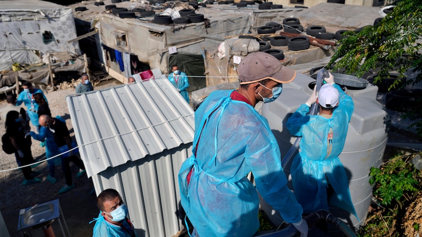 Workers in protective gear carry a hose to a water tank. 