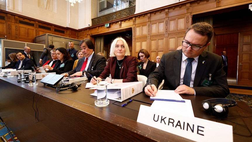 Courtroom panel, headed by a sign that says Ukraine 