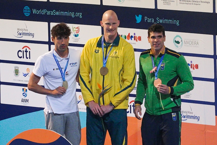 Three para swimming athletes pose with their medals after a race