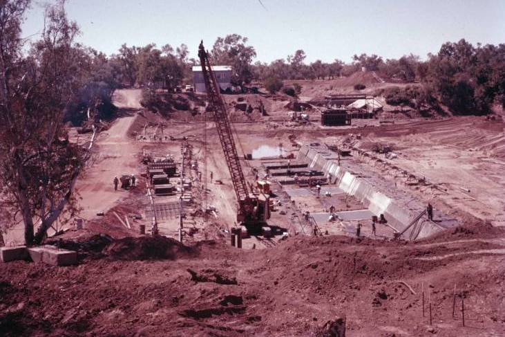 a sepia toned photo of men and cranes in a dusty and concrete filled creek