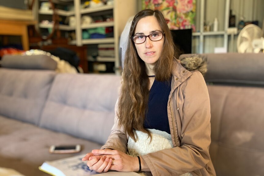 A woman with long-dark hair and glasses sits on a lounge in a shed.