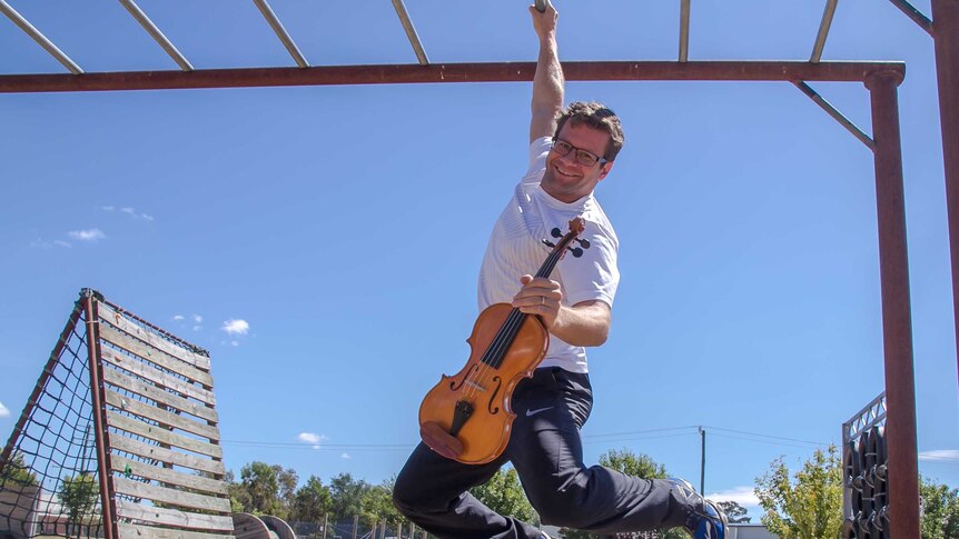 A man hanging from a jungle gym holding a violin