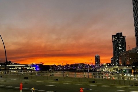 Smoky Brisbane city sunset with orange sky and trees on the right of the frame